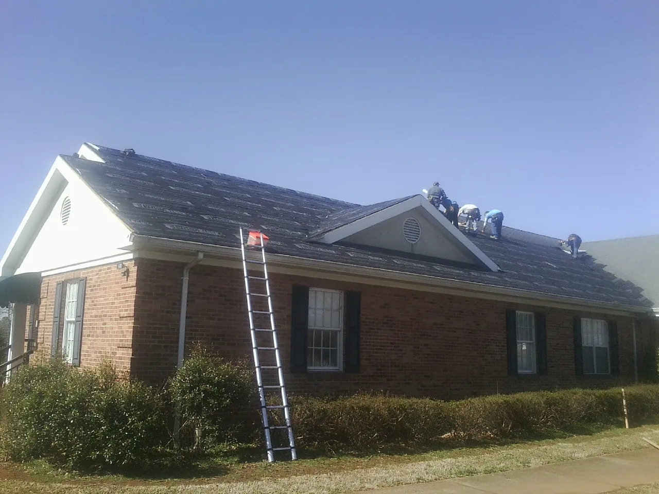 Crew tearing shingles off a brick ranch roof with a ladder set — Metal Roof Repair work by our crew in Walford