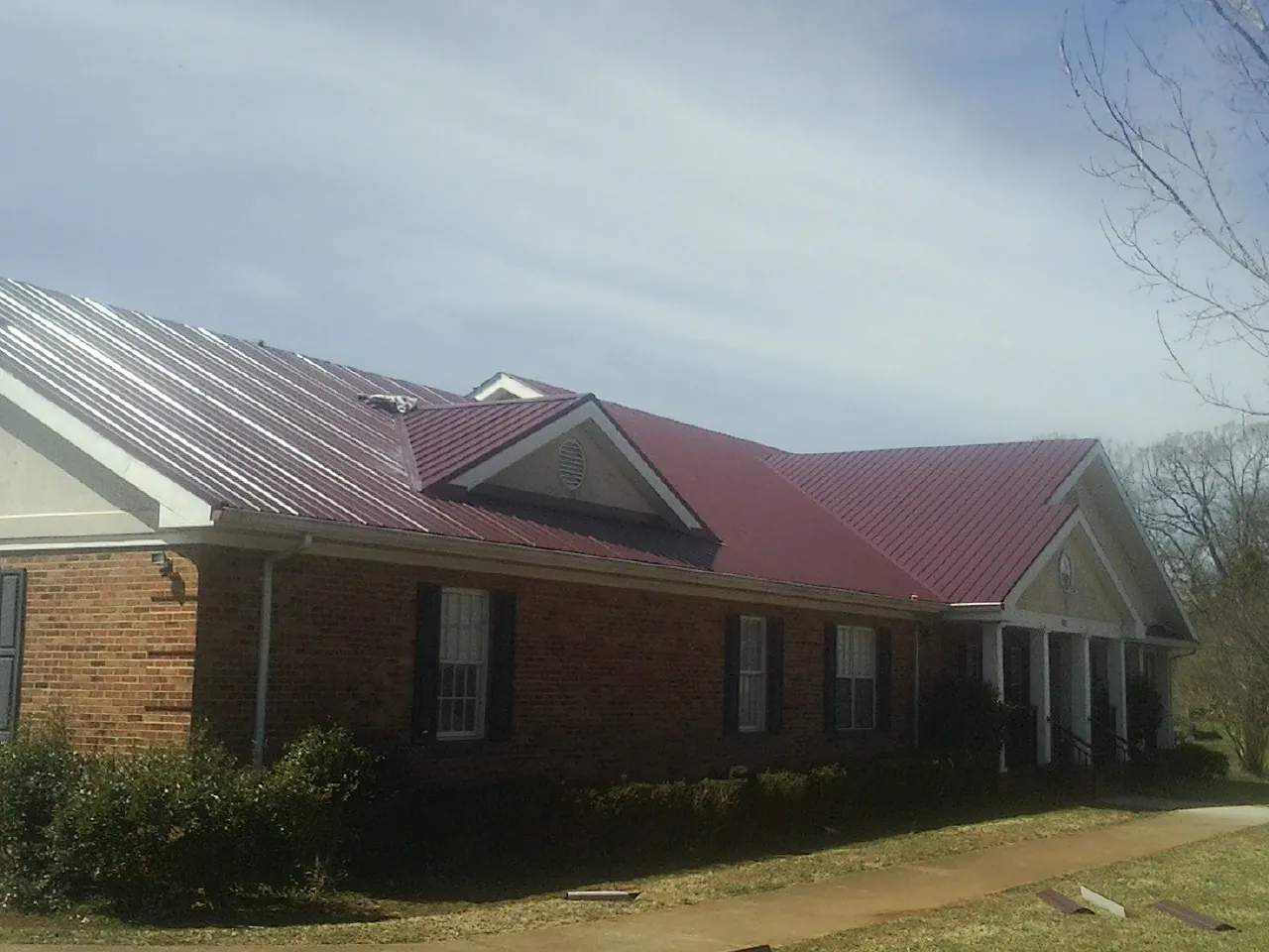 Red metal roof with gabled entries on a long brick building, from a Hail Damage Roof Repair job in Walford