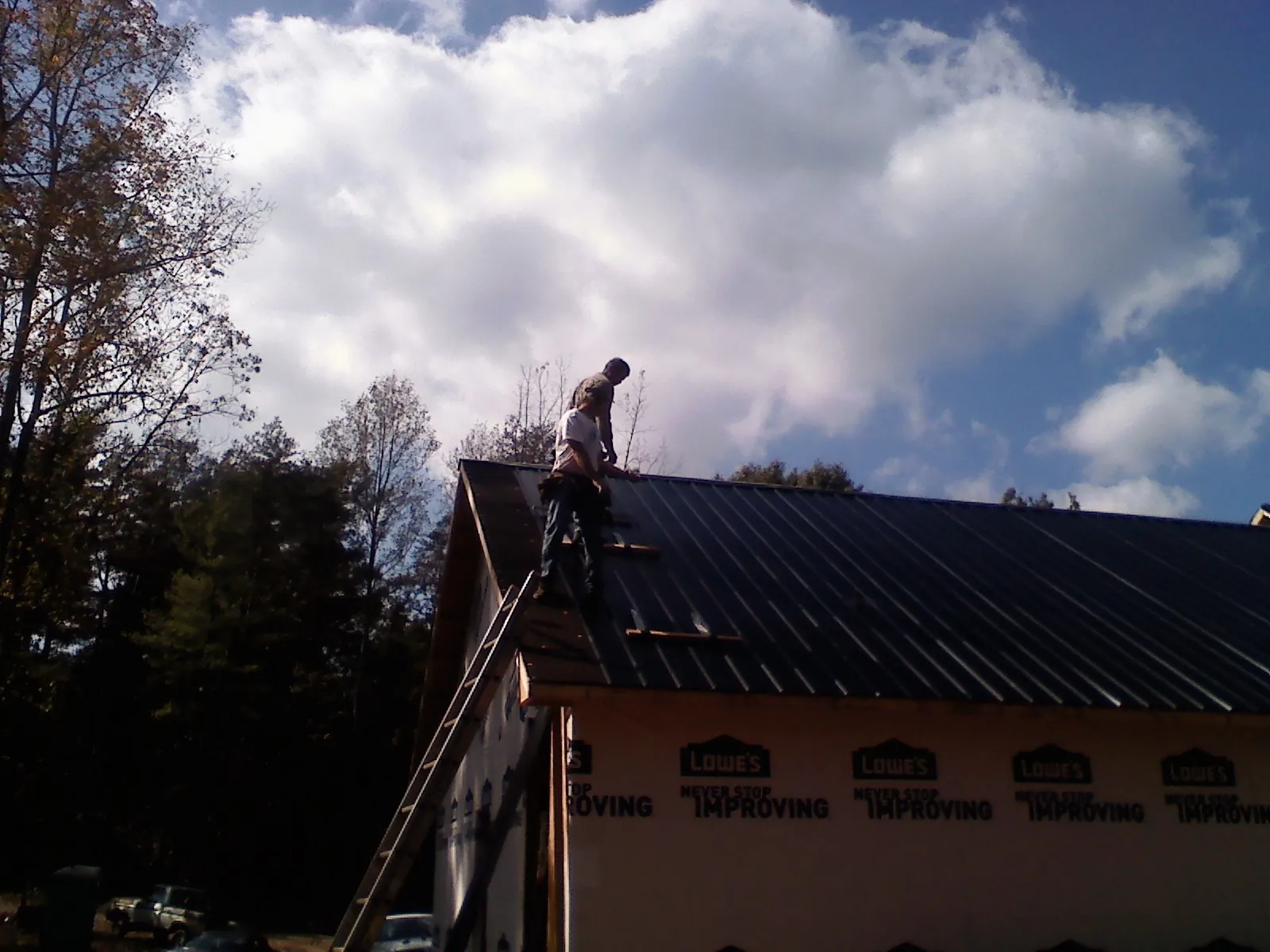 Roofer fastening dark metal panels high against a cloudy sky, from a Roof Inspection job in Walford
