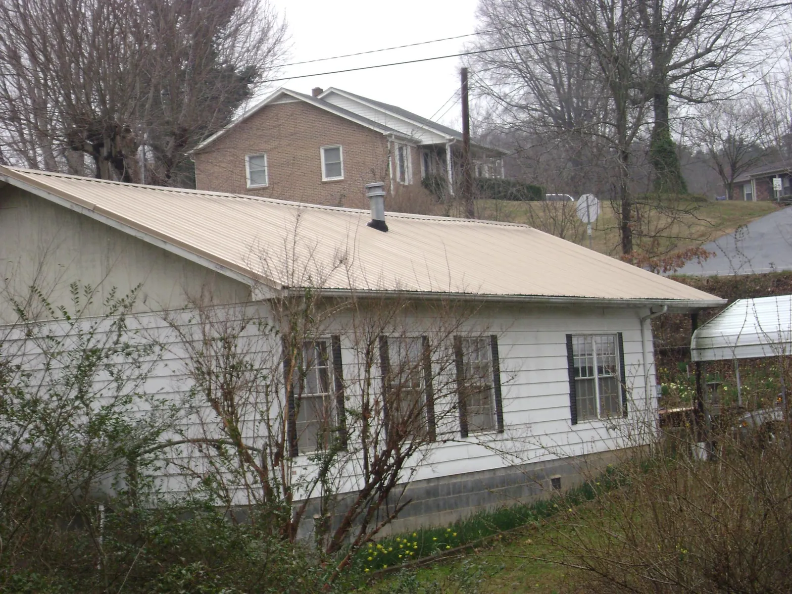Tan metal roof on a white sided house set into a hillside — Commercial Roofing by Roofing Brothers in Walford
