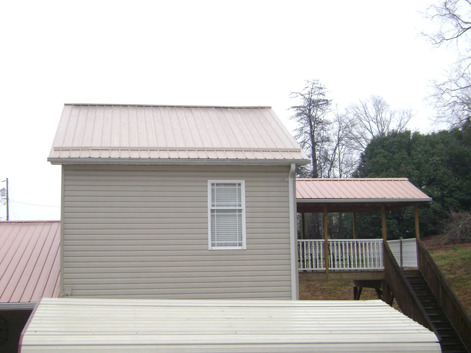 Tan metal roofs on a two story addition and attached porch, from a Roof Replacement job in Walford